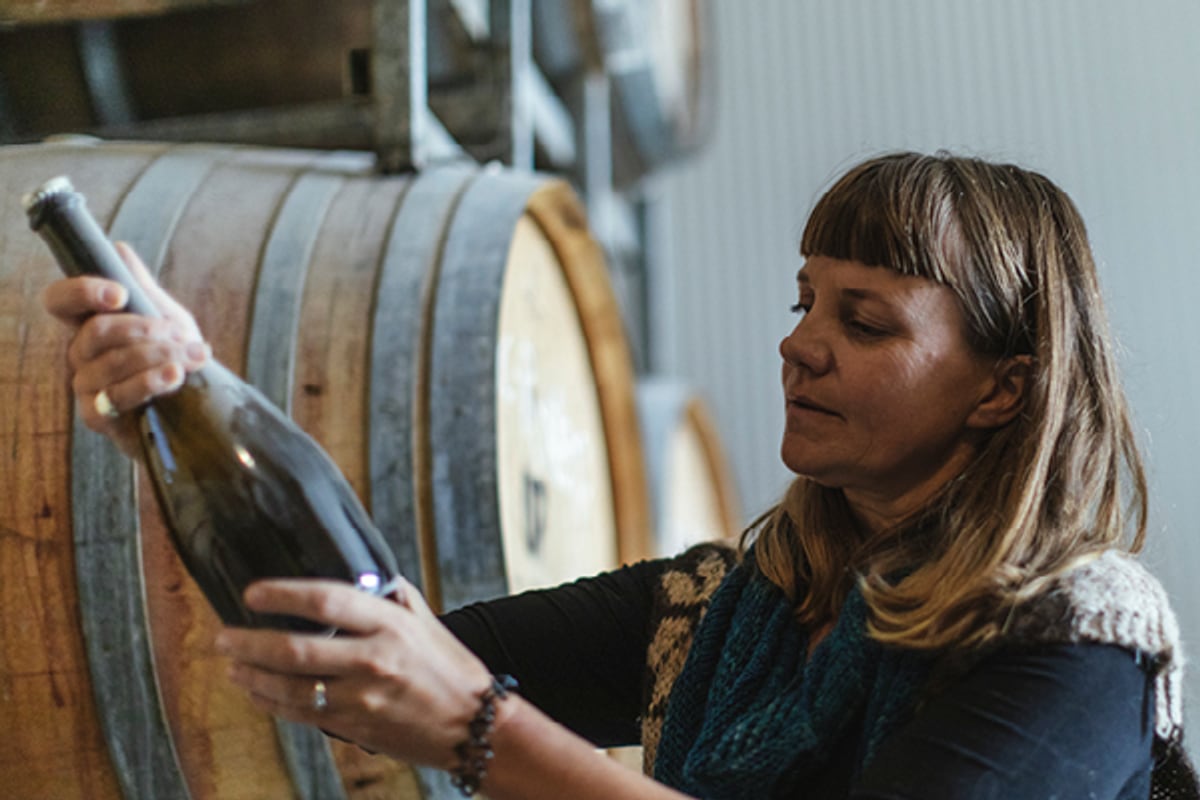 A winemaker examining a bottle beside oak barrels in an Australian winery